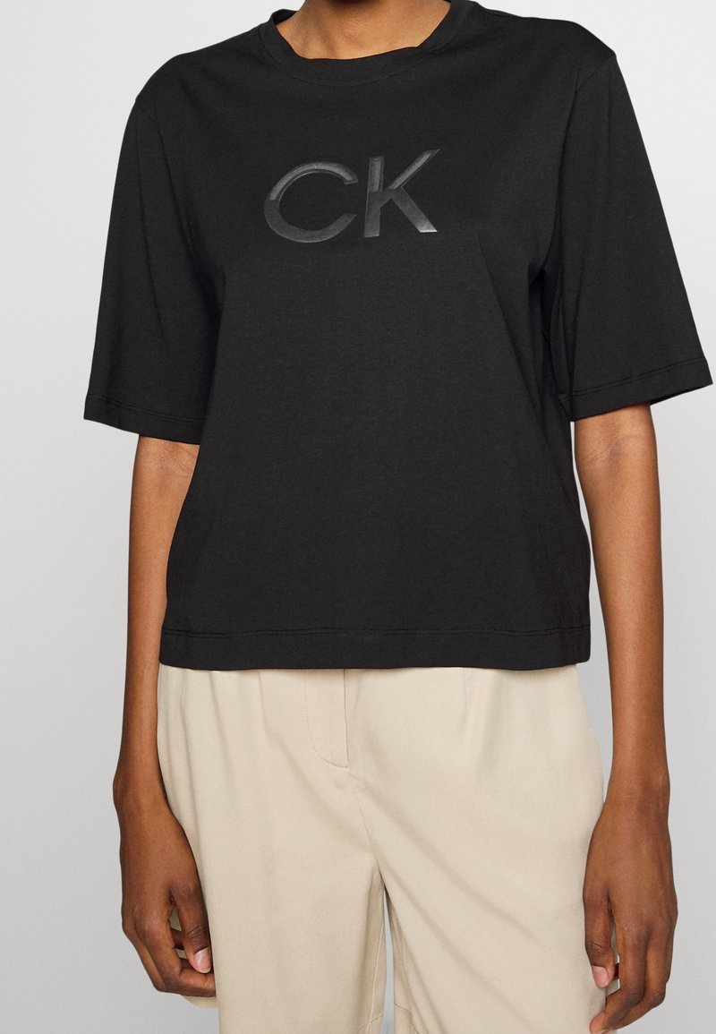 Sort bomulds t-shirt med korte ærmer, der har et skinnende sort "CK" logo på forsiden. Simpelt design, afslappet pasform.