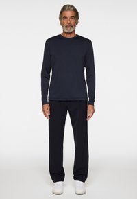 Marinblus med lång ärm i kombination med svarta byxor, gjorda av ett slätt material. Modellen bär vita sneakers. Enkel, åtsittande design utan mönster.