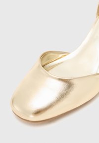 Scarpa slip-on metallica oro con punta quadrata, texture liscia e design minimalista. L'interno presenta una fodera lucida.