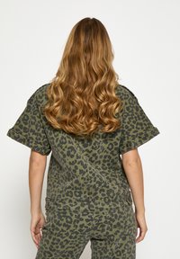 Leopardenmuster-Jumpsuit in Grün und Schwarz, mit kurzen Ärmeln, weiter Passform und sichtbaren Nahtdetails am Stoff.