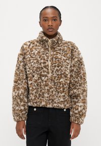 Bruine en crèmekleurige zachte trui met hoge kraag, halve ritssluiting aan de voorkant en een textuurstof met een patroon van verschillende tinten bruin.