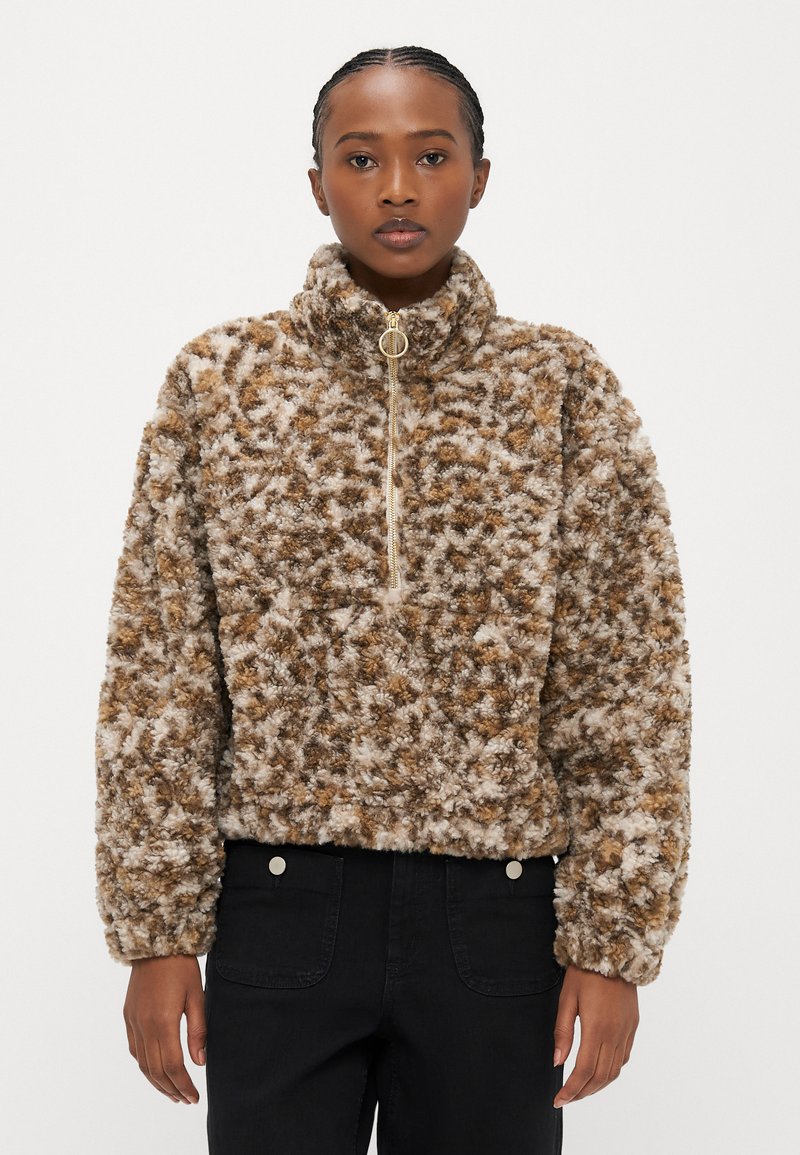 Bruine en crèmekleurige zachte trui met hoge kraag, halve ritssluiting aan de voorkant en een textuurstof met een patroon van verschillende tinten bruin.