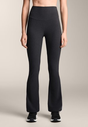 Colanți negri evazați pentru sport, cu talie înaltă, realizați dintr-un material neted și elastic, asortați cu pantofi sport negri.