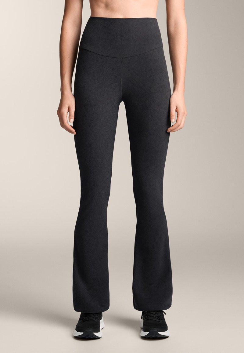 Zwarte uitlopende sportlegging met een hoge tailleband, gemaakt van een glad, rekbaar materiaal, gecombineerd met zwarte sportschoenen.