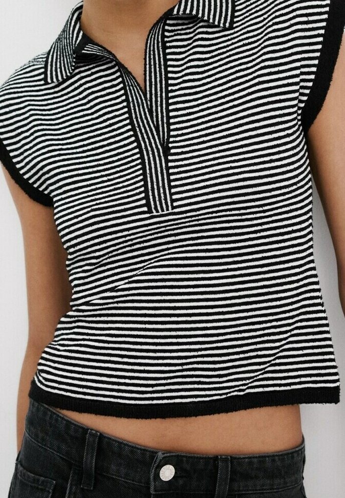 Haut en maille sans manches à rayures horizontales noires et blanches avec col et patte de boutonnage partielle, porté avec un jean noir.
