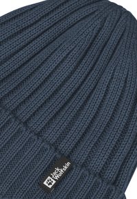 Berretto lavorato a maglia blu scuro con texture a costine. Presenta un'etichetta nera con testo e logo bianchi ricamati sul bordo.