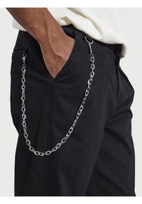 Catena metallica attaccata a pantaloni neri, con maglie arrotondate e un gancio. La catena pende liberamente lungo l'area della tasca laterale.