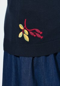 Marineblauwe truizoom met een geborduurde tak met rode bessen en geelgroene bladeren, gedragen over een blauwe denim rok.