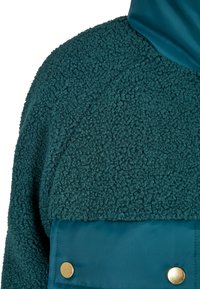 Veste en polaire teal avec une section supérieure texturée et un panneau inférieur lisse et brillant. Comprend des boutons pression dorés sur la section inférieure.