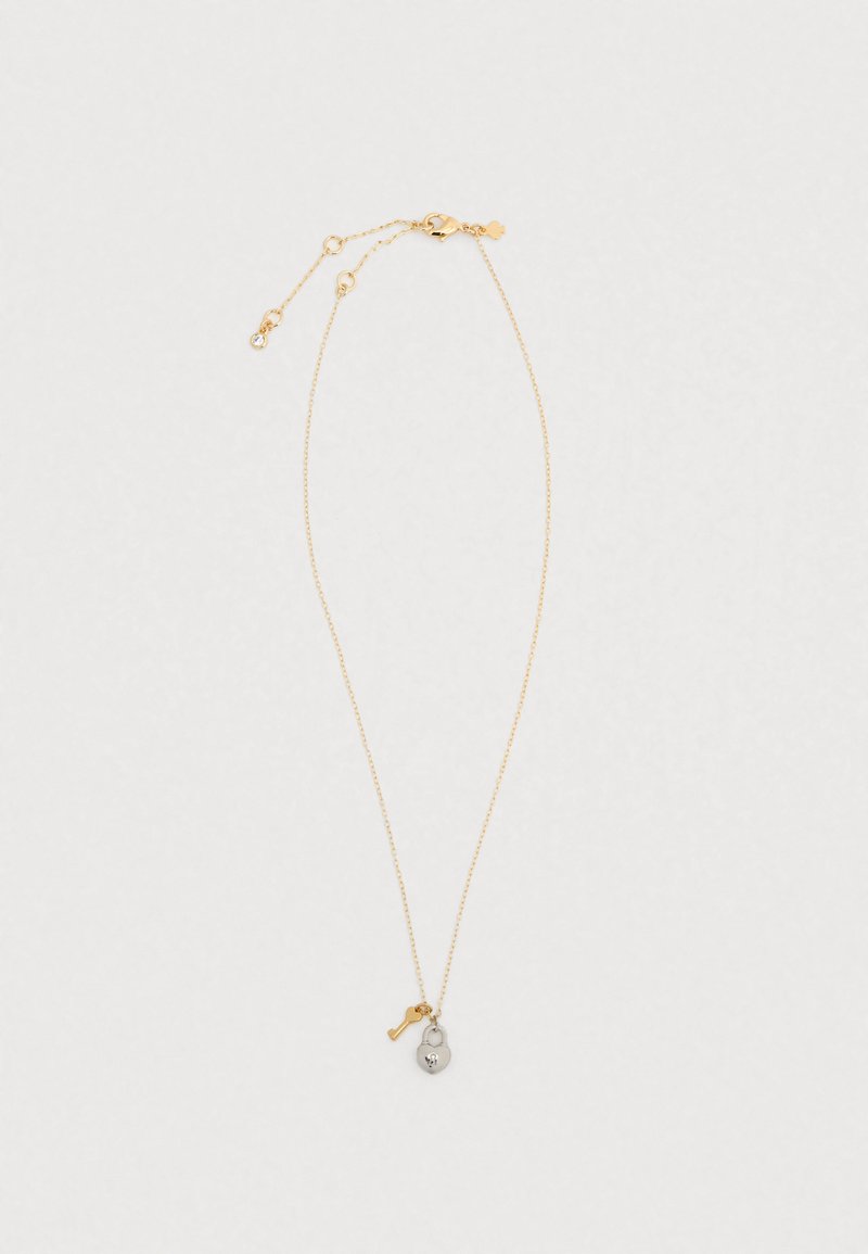 Κολιέ με χρυσή αλυσίδα που διαθέτει ένα μικρό φυλαχτό σε σχήμα καρδιάς με λεπτομέρειες κρανίου και έμφαση σε κλειδί. Η αλυσίδα έχει λεπτή υφή.