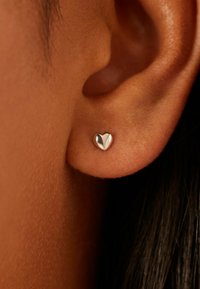 Silver heart-shaped stud earring with a polished finish, featuring a smooth surface and compact design, showcased against an ear.