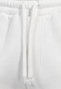 Pantalones de chándal blancos de algodón con cordón y tejido texturizado. Presenta bolsillos laterales y una cinturilla acanalada para mayor comodidad.