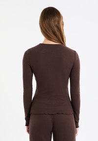 Braunes, geripptes Langarmoberteil mit geschwungenem Saum und figurbetontem Design aus elastischem Stoff, Rückansicht.