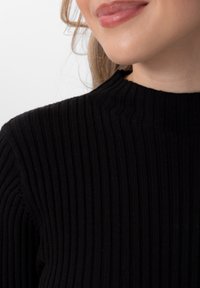 Pull à col roulé noir côtelé avec un motif de tricot texturé. L'encolure présente un détail subtil et légèrement en relief. Tissu doux avec une silhouette ajustée.