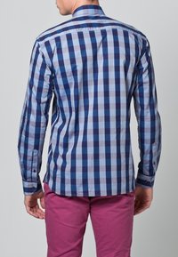 Niebieska i jasno-niebieska koszula w kratę z długim rękawem, kołnierzykiem zapinanym na guziki oraz kontrastującymi ciemnymi guzikami, zestawiona z różowymi spodniami.