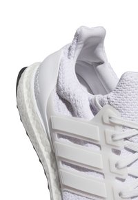 Białe sneakersy sportowe wykonane z materiału dzianinowego, z trzema solidnymi białymi paskami i teksturowaną białą podeszwą, posiadające wyściółkę w okolicy kostki oraz sznurowanie.