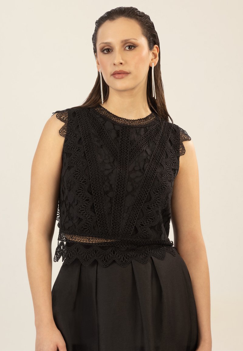 Top de encaje negro con patrones intrincados, bordes ondulados y un diseño ajustado, combinado con una falda negra fluida para un look cohesivo.