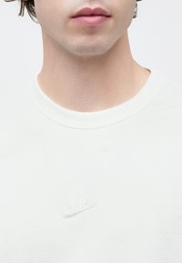 Λευκό βαμβακερό μπλουζάκι με στρογγυλή λαιμόκοψη και λεπτό ανάγλυφο λογότυπο της Nike στο στήθος. Μαλακό ύφασμα με λεία υφή.