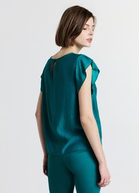 Haut à manches courtes bleu sarcelle avec tissu texturé, encolure ronde et un détail en forme de goutte d'eau dans le dos. Associé à un pantalon bleu sarcelle assorti.