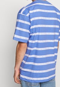 Blå randig t-shirt med horisontella vita band som har en handskriven logotyp. Kort ärm, bomullsmaterial, avslappnad passform och rund hals.