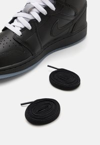 Czarny wysoki sneaker ze skóry z białymi sznurowadłami, perforowanym noskiem i kontrastującą gumową podeszwą. Zawiera dwie czarne, okrągłe sznurowadła.