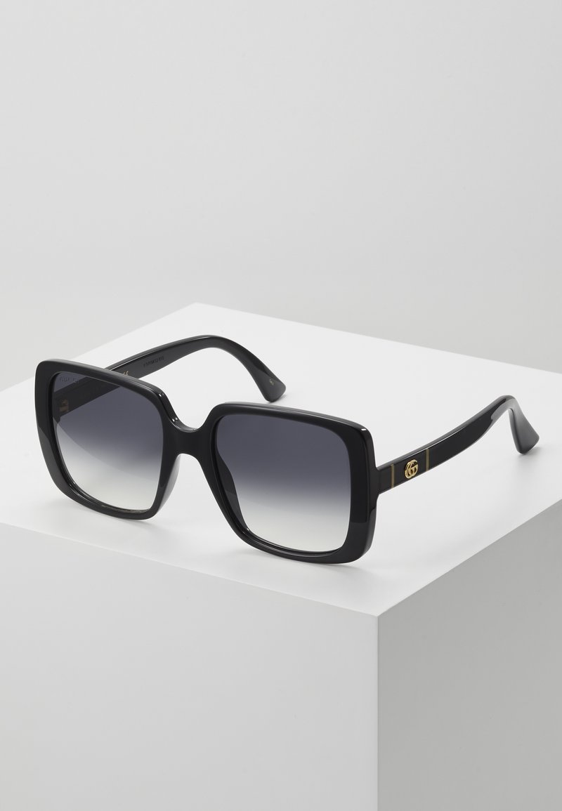 Black square sunglasses with gradient lenses. Glossy plastic frames. Features gold hardware accents on the temples.