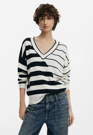 V-Ausschnitt Strickpullover mit breiten Navy- und Creme-Streifen, mit überschnittenen Schultern und einer lockeren Passform, kombiniert mit hochgeschnittenen Jeans.