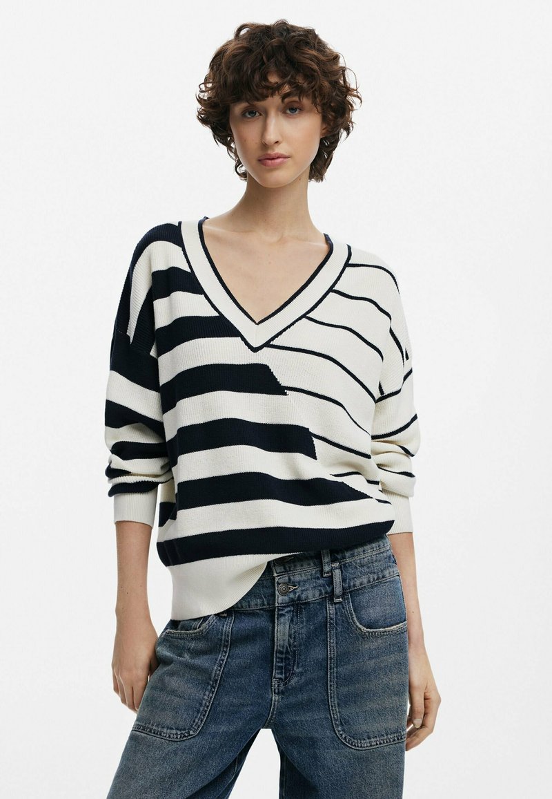 Maglione a scollo a V lavorato a maglia con ampie righe blu navy e crema, con spalle scese e una vestibilità rilassata, abbinato a jeans in denim a vita alta.