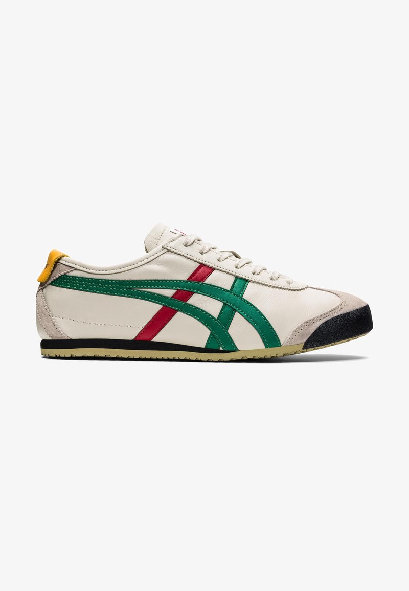 Baskets blanches discrètes avec des rayures vertes et rouges, bout en daim beige, bord de semelle noire, languette de talon jaune et lacets blancs sur fond blanc.