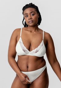 Weißer Bralette mit Spitzenrand, verstellbaren Trägern und V-Ausschnitt. Weicher Stoff mit glatter Textur. Passender weißer Bikiniunterteil.