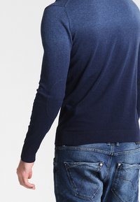 Mörkblå stickad tröja med en slät yta, ribbade ärmslut och rundad nederkant. Har även armbågsfickor och en gradientdesign upp mot toppen.