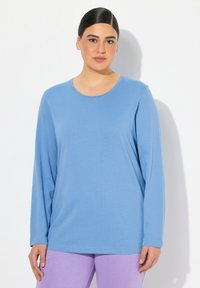 Světle modrý dlouhý rukáv top s kulatým výstřihem, vyrobený z měkké tkaniny. Nosí se s levandulovými kalhotami, které mají volný střih a hladkou texturu.