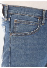 Blå denimjeans med en klassisk femficksdesign, kontrasterande sömmar och en liten myntficka på framsidan till höger.