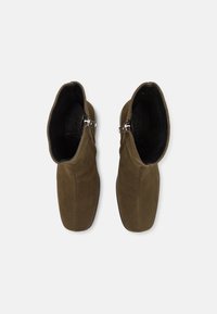 Botas de tobillo de ante verde aceituna con una textura suave, que cuentan con un acento de hebilla plateada y un diseño de punta redondeada. El interior es negro.