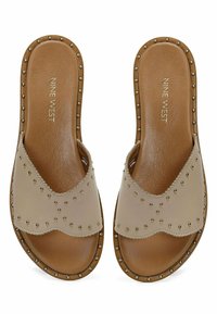 Beige slidesandaler med en tekstureret læderoverdel, bølgekant, dekorative gyldne nitter og en glat brun indersål.