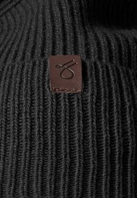 Black knitted sweater featuring a ribbed texture. A brown leather label with a stitching accent is visible on the collar.