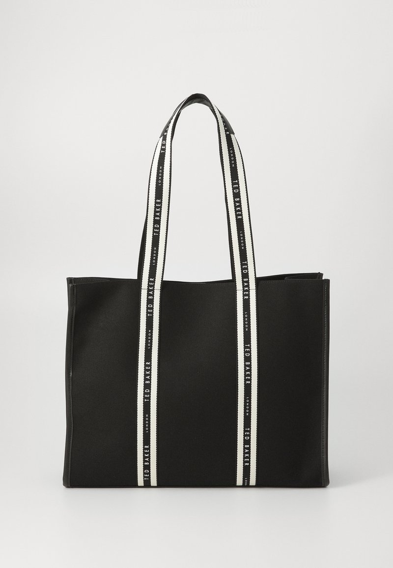 Mustan kangaskassi, jossa on teksturoitu pinta, varustettuna kahdella tukevalla musta-valkoisella raidallisella sangalla. Brändin nimi painettuna hihnojen varrelle. Suorakaiteen muotoinen muotoilu.