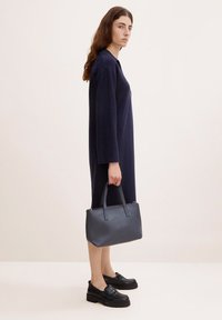 Abito lavorato a maglia di colore navy con maniche lunghe, abbinato a una borsa nera strutturata e a scarpe nere spesse. Silhouette semplice ed elegante.
