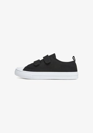Zapatilla deportiva de lona negra con dos tiras de velcro, puntera de goma blanca y suela blanca. Cuenta con una lengüeta en la parte trasera para facilitar su colocación.