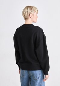 Svart oversized hettegenser med rund hals og senkede skuldre, kombinert med lyseblå denimjeans. Glatt tekstur og avslappet passform.