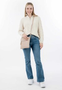 Maglione beige a trecce con colletto zip, jeans blu a zampa d'elefante e borsa a tracolla beige. Sneakers bianche completano l'outfit.