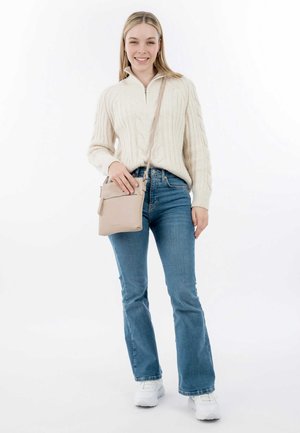Maglione beige a trecce con colletto zip, jeans blu a zampa d'elefante e borsa a tracolla beige. Sneakers bianche completano l'outfit.