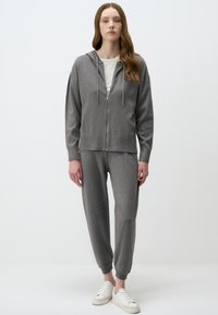 Sweat à capuche zippé gris avec une capuche et des cordons de serrage, associé à un pantalon de survêtement slim assorti. Présente une texture douce et une coupe décontractée.