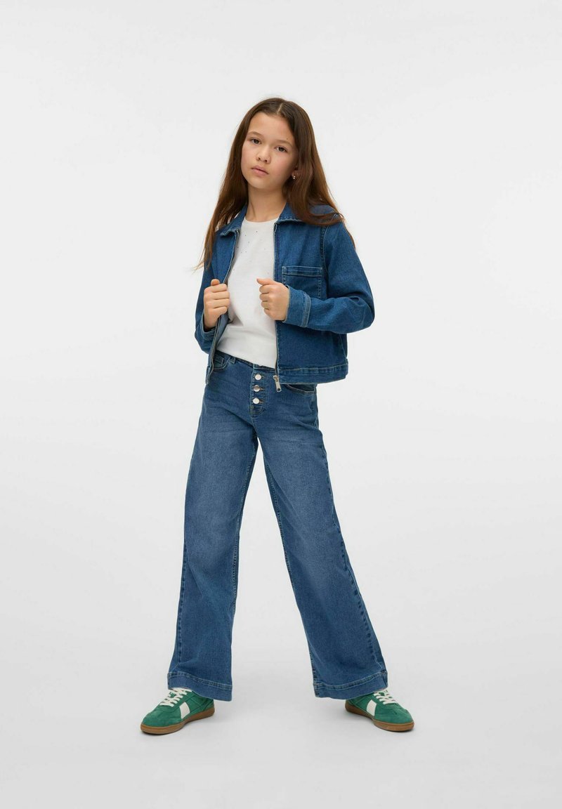 Jeansjacka och högmidjade utsvängda jeans i mellanblått, stiliserat med en vit T-shirt och gröna träningsskor med vita accenter.