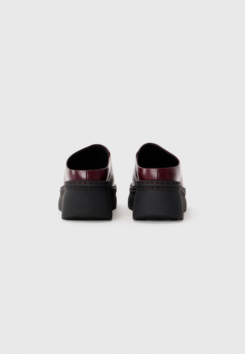 Bordeaux leren schoenen met een afgeronde achterkant, zwarte rubberen zool en gestikte details langs de middenzool. Vlotte textuur, modern ontwerp.