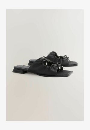 Čierne sandále na opätku so štruktúrovaným textilným zvrškom, s dvoma mašľami a kovovými detailmi. Plná podrážka a štvorcový tvar špičky.