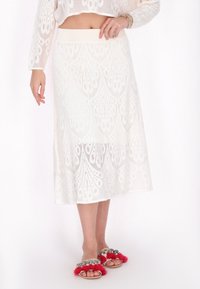 Hvid blonde midi-nederdel med blomstermønster, elastisk talje og gennemsigtig tekstur, kombineret med sandaler med lyserøde kvaster og dekorative detaljer.