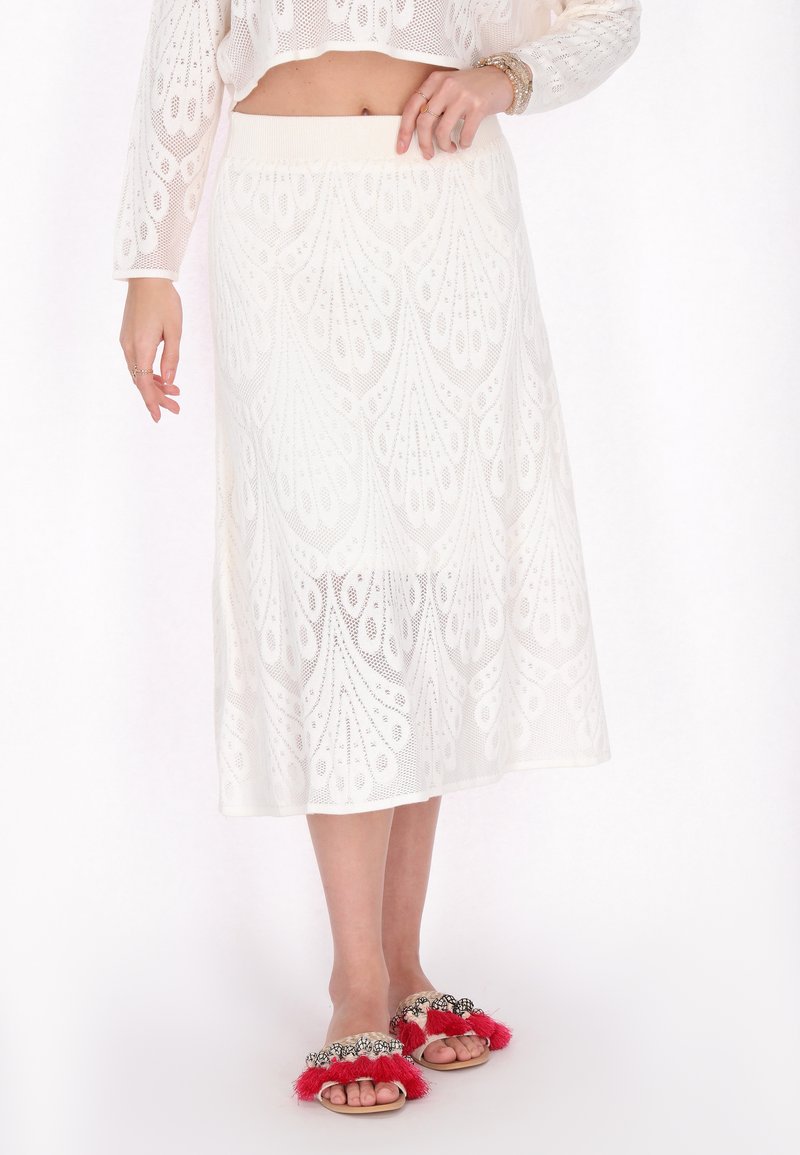 Hvid blonde midi-nederdel med blomstermønster, elastisk talje og gennemsigtig tekstur, kombineret med sandaler med lyserøde kvaster og dekorative detaljer.