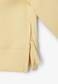 Gelbes Sweatshirt mit weicher Textur, seitlichen Schlitzen und einem Reißverschlussdetail am Saum. Glattes Material mit einem schlichten Design.