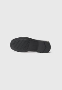 Semelle de chaussure noire avec motifs de grip texturés, taille 37 en relief, et nom de la marque visible sur le dessous.
